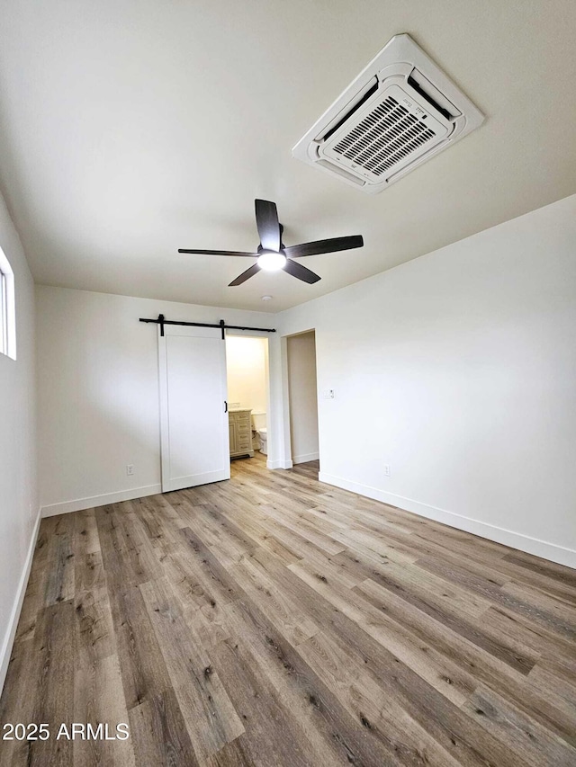 unfurnished bedroom with a barn door, light wood-style flooring, visible vents, a ceiling fan, and baseboards