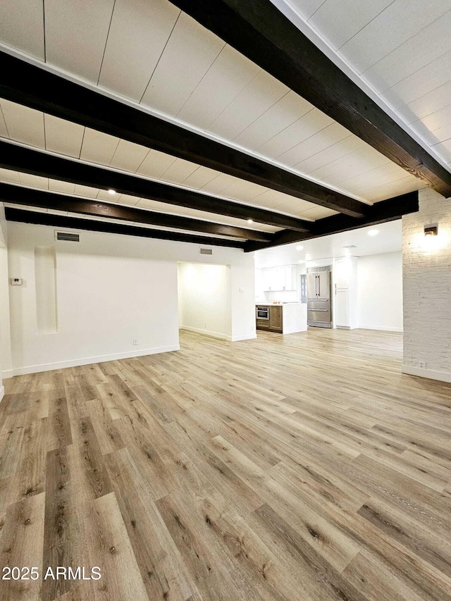 unfurnished living room featuring light wood-style floors, visible vents, baseboards, and beam ceiling