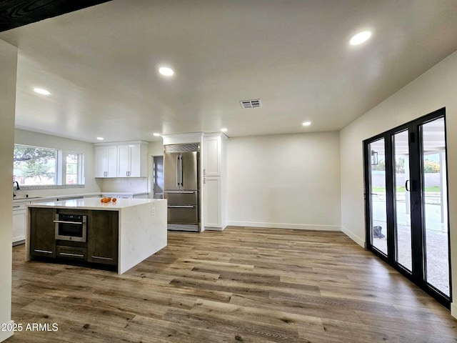 kitchen with built in refrigerator, wood finished floors, visible vents, white cabinetry, and light countertops