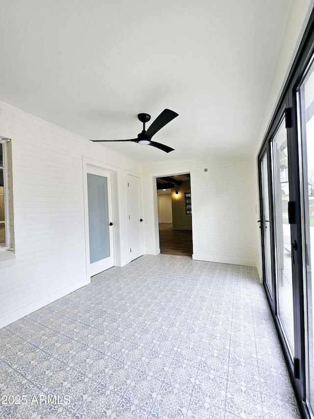 spare room featuring ceiling fan and brick wall