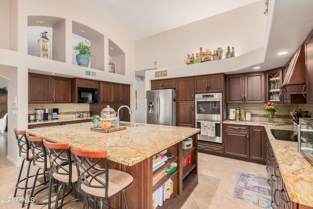 kitchen with light stone countertops, light tile patterned floors, black appliances, a center island with sink, and sink