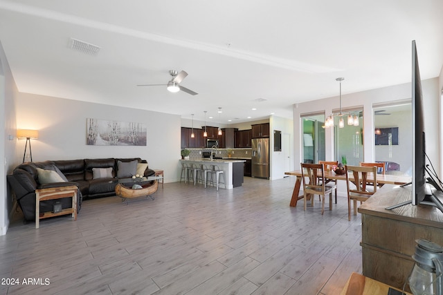 living room featuring ceiling fan with notable chandelier and light wood-type flooring