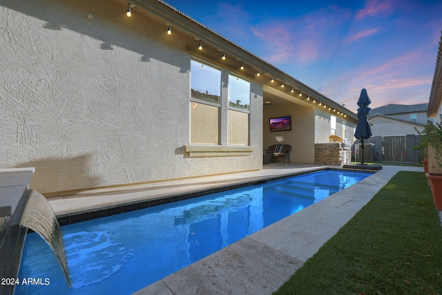 pool at dusk with a patio area and a yard