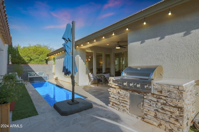 patio terrace at dusk with area for grilling, ceiling fan, and exterior kitchen