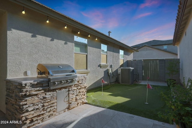 patio terrace at dusk with central air condition unit, an outdoor kitchen, and grilling area