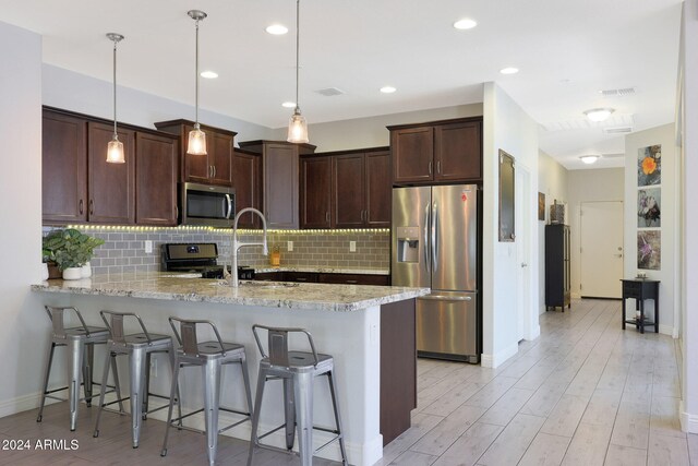 kitchen featuring pendant lighting, light hardwood / wood-style floors, appliances with stainless steel finishes, and kitchen peninsula