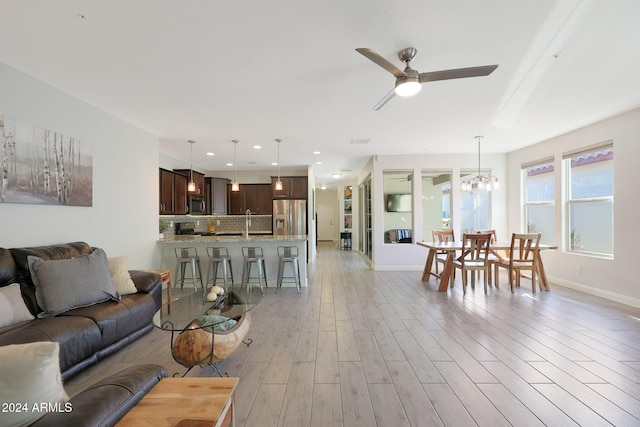 living room with sink, light hardwood / wood-style flooring, and ceiling fan with notable chandelier