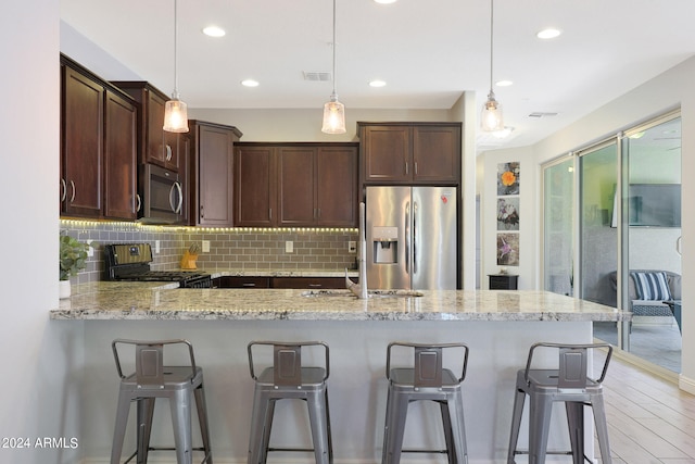 kitchen featuring appliances with stainless steel finishes, light wood-type flooring, backsplash, decorative light fixtures, and light stone counters