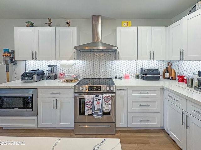 kitchen featuring white cabinetry, wall chimney range hood, appliances with stainless steel finishes, and tasteful backsplash