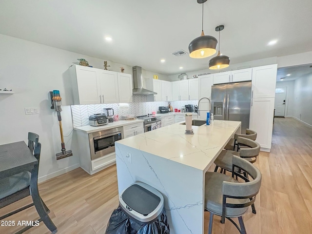 kitchen with backsplash, stainless steel appliances, wall chimney range hood, pendant lighting, and white cabinets