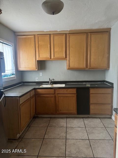 kitchen featuring a sink, light tile patterned flooring, dark countertops, and brown cabinets