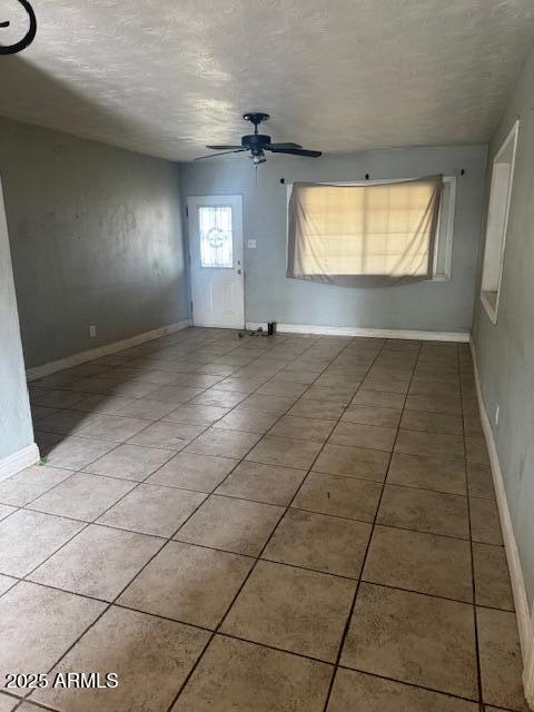 empty room featuring a textured ceiling, a ceiling fan, tile patterned flooring, and baseboards