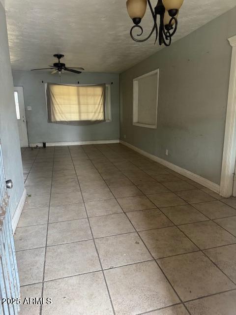 empty room with light tile patterned floors, ceiling fan, a textured ceiling, a chandelier, and baseboards