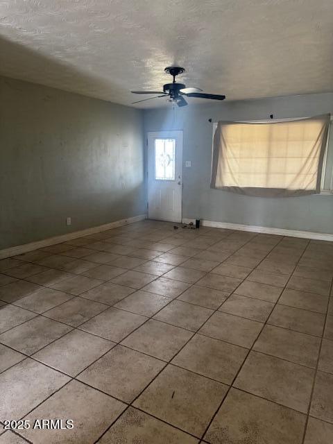 spare room with tile patterned flooring, ceiling fan, a textured ceiling, and baseboards