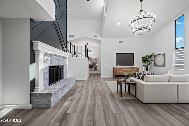 living room featuring light hardwood / wood-style floors, an inviting chandelier, a high ceiling, and a brick fireplace