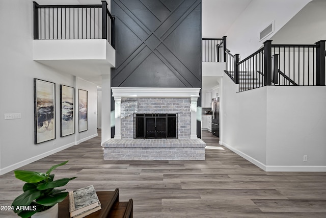 living room with hardwood / wood-style floors, a towering ceiling, and a brick fireplace