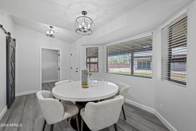 dining room with a notable chandelier, a barn door, wood-type flooring, and vaulted ceiling