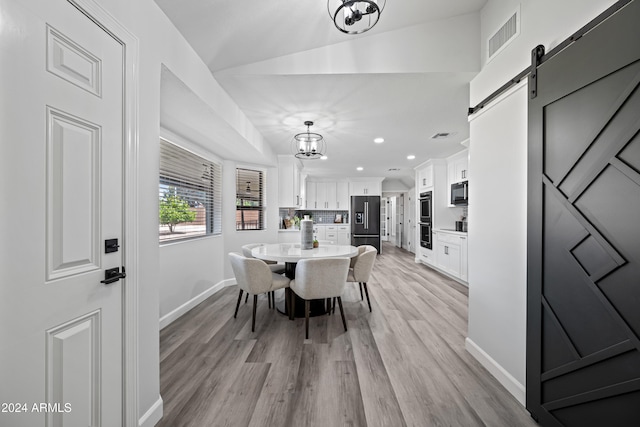 dining room featuring a chandelier, a barn door, light hardwood / wood-style floors, and vaulted ceiling