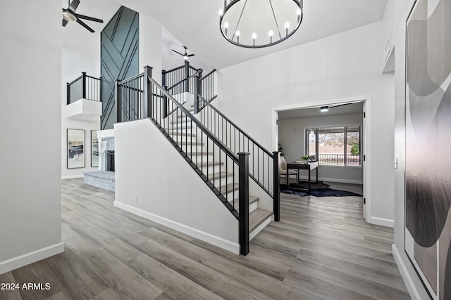 stairs featuring a fireplace, ceiling fan with notable chandelier, and hardwood / wood-style flooring