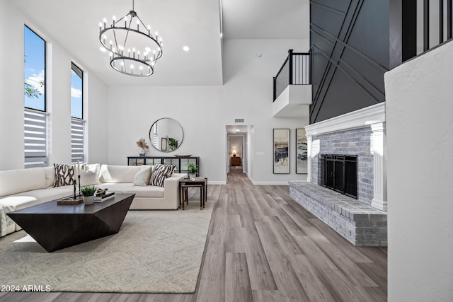 living room featuring a notable chandelier, a towering ceiling, a fireplace, and light hardwood / wood-style flooring