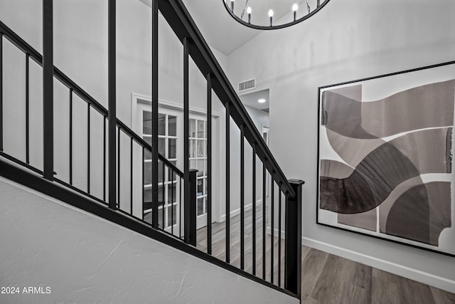 stairs featuring hardwood / wood-style flooring, high vaulted ceiling, and a chandelier