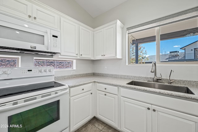 kitchen featuring sink, light tile patterned flooring, vaulted ceiling, white appliances, and white cabinets