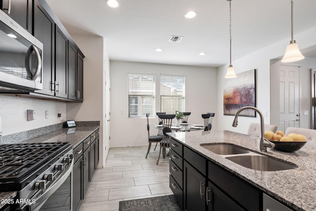 kitchen featuring light stone counters, appliances with stainless steel finishes, decorative light fixtures, and sink