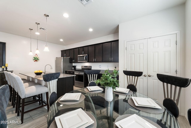 kitchen with sink, a breakfast bar area, hanging light fixtures, stainless steel appliances, and an island with sink