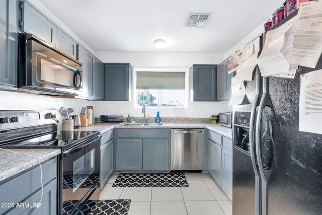 kitchen with gray cabinets, sink, light tile patterned floors, stainless steel appliances, and light stone countertops