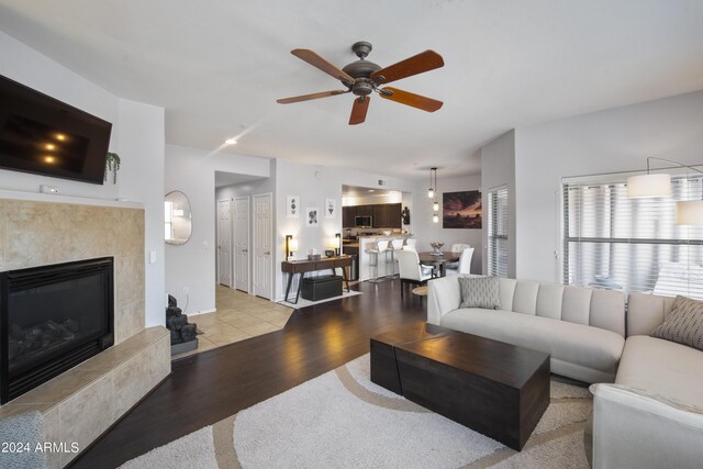 living room with ceiling fan, light hardwood / wood-style flooring, and a tiled fireplace