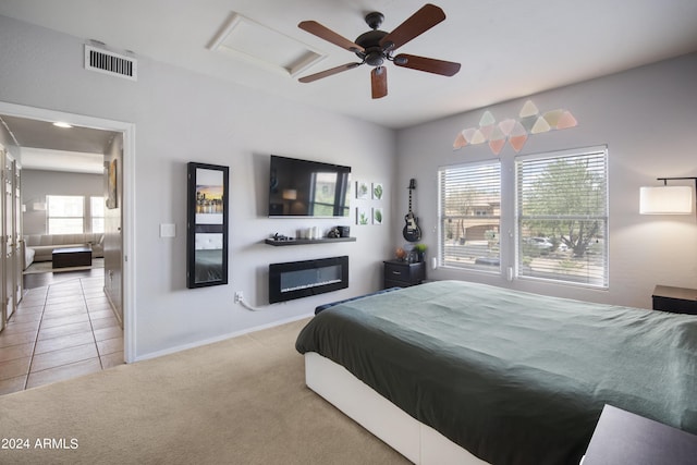 bedroom featuring visible vents, a ceiling fan, a glass covered fireplace, light colored carpet, and light tile patterned flooring