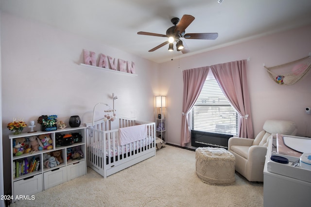 bedroom featuring a nursery area, light carpet, and a ceiling fan