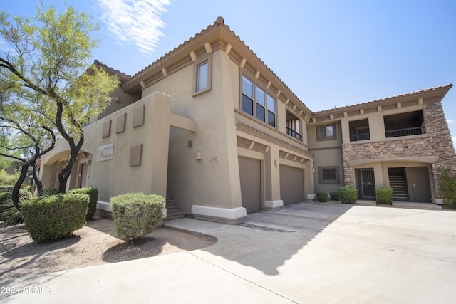 view of front of house with an attached garage, a tile roof, stone siding, concrete driveway, and stucco siding