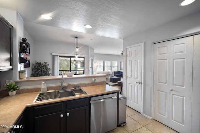 kitchen featuring light countertops, hanging light fixtures, stainless steel dishwasher, a sink, and dark cabinets