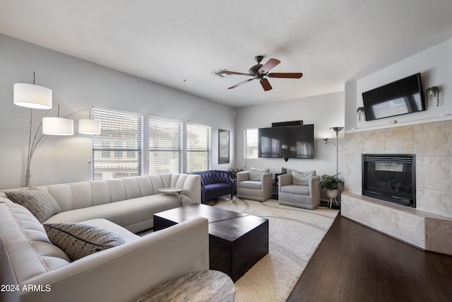 living room with ceiling fan, a tiled fireplace, visible vents, and wood finished floors