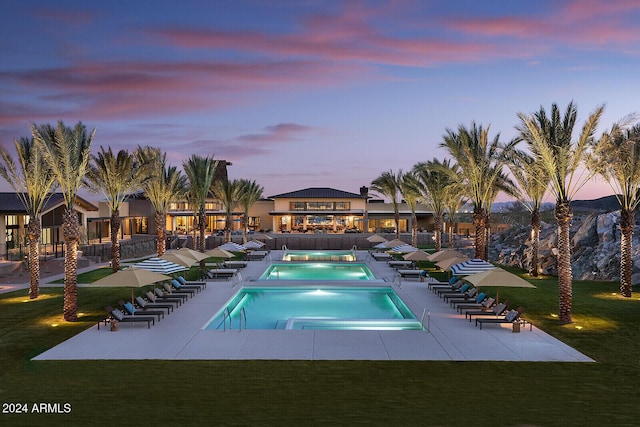 pool at dusk featuring a jacuzzi, a patio, a yard, and a community pool