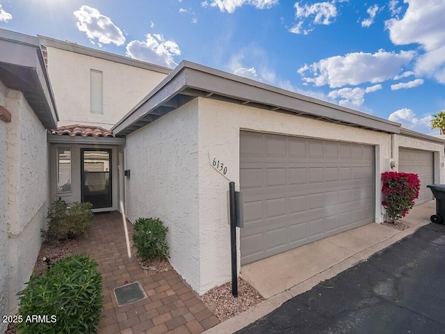 exterior space featuring an attached garage, aphalt driveway, a tile roof, and stucco siding