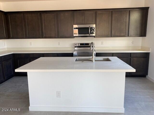 kitchen featuring sink, stainless steel appliances, dark brown cabinets, a center island with sink, and dark tile patterned flooring