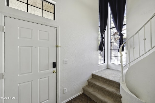 entrance foyer with a textured wall, baseboards, and stairs