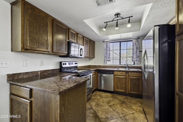 kitchen featuring visible vents, dark countertops, appliances with stainless steel finishes, a tray ceiling, and a sink