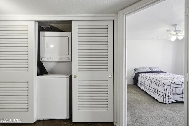 laundry room featuring laundry area, ceiling fan, stacked washer / drying machine, dark colored carpet, and a textured ceiling