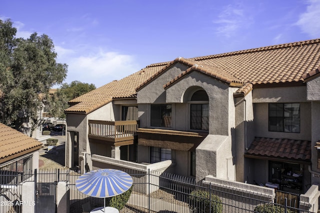 exterior space featuring a tiled roof, a fenced front yard, a balcony, and stucco siding