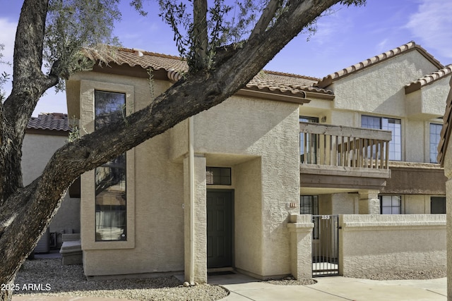 exterior space with a fenced front yard, a balcony, a tile roof, a gate, and stucco siding