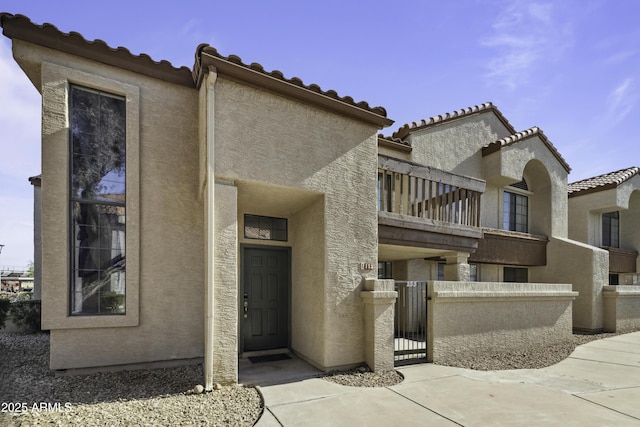 exterior space with stucco siding, a gate, fence, a balcony, and a tiled roof