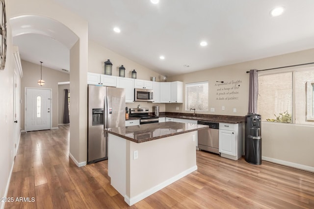 kitchen with arched walkways, lofted ceiling, a sink, white cabinetry, and appliances with stainless steel finishes