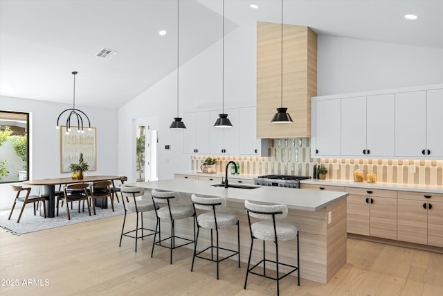 kitchen featuring light wood finished floors, an island with sink, light countertops, a kitchen bar, and a sink