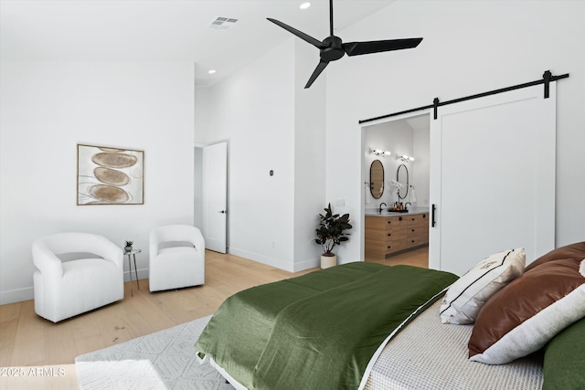 bedroom with visible vents, a barn door, high vaulted ceiling, light wood-type flooring, and baseboards