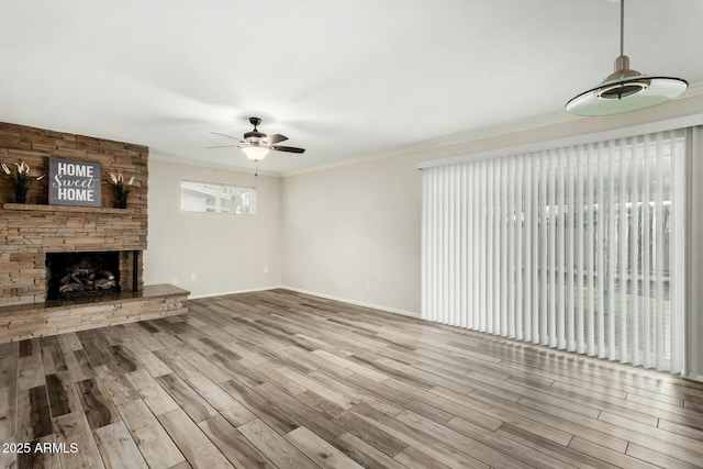 unfurnished living room with ceiling fan, a stone fireplace, wood finished floors, and crown molding