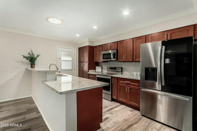 kitchen with light wood finished floors, a peninsula, stainless steel appliances, and a sink