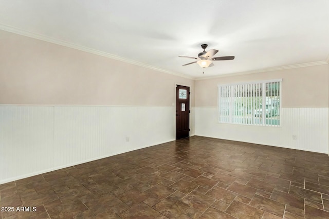 empty room featuring a wainscoted wall, stone finish floor, a ceiling fan, and ornamental molding